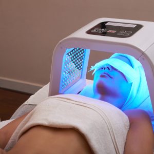 Young woman having LED light facial treatment in beauty salon